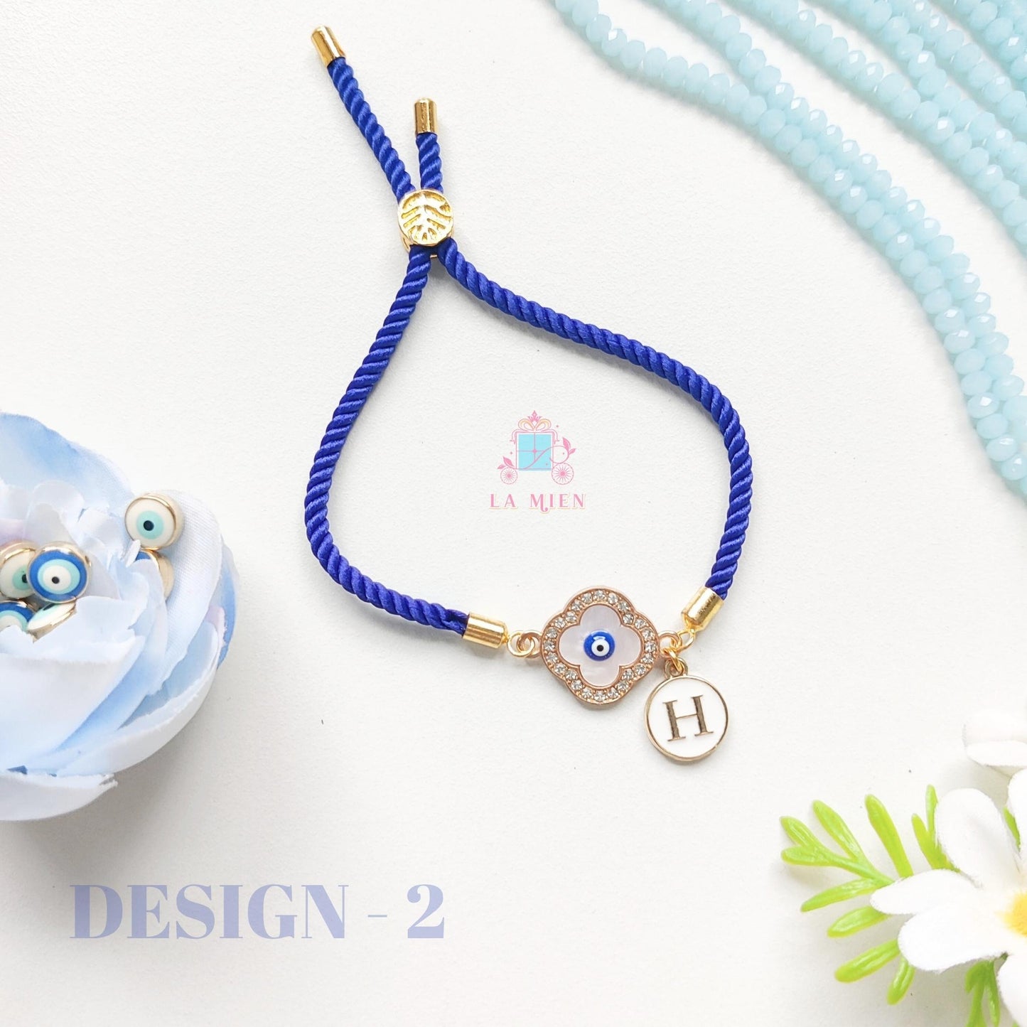 Evil eye rakhi bracelet with custom initial tag and adjustable blue cord.