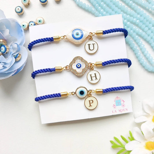 Set of 3 personalized evil eye rakhi bracelets with initial charms and adjustable blue cords.